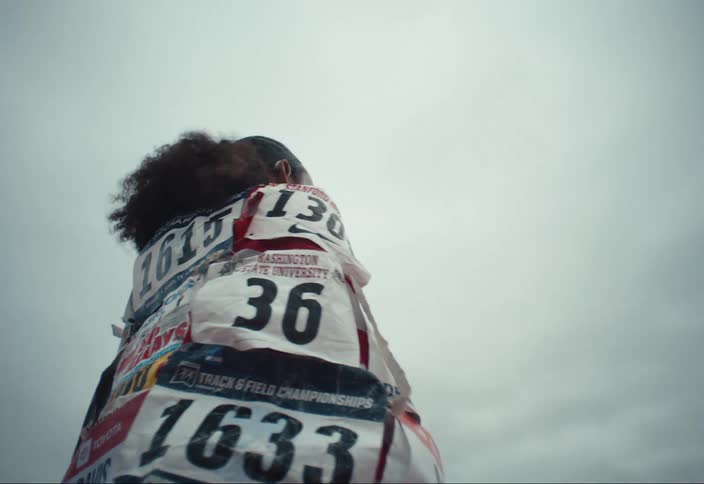 A woman standing outdoors wearing a flag covered in tags from running races