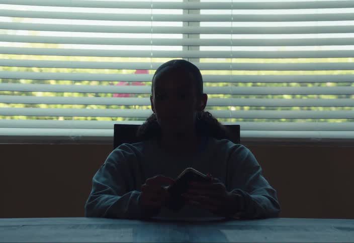 A young woman sitting at the kitchen table holding her phone
