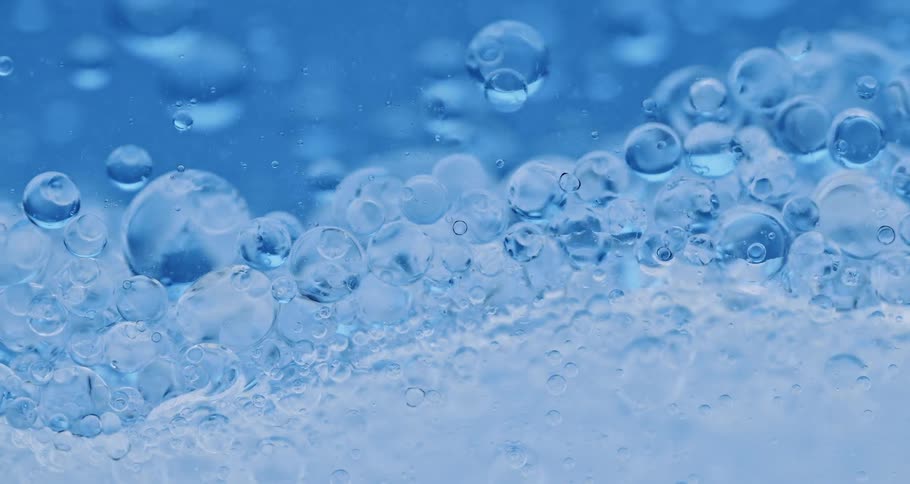 Clear blue oily bubbles forming together in a liquid against a glass