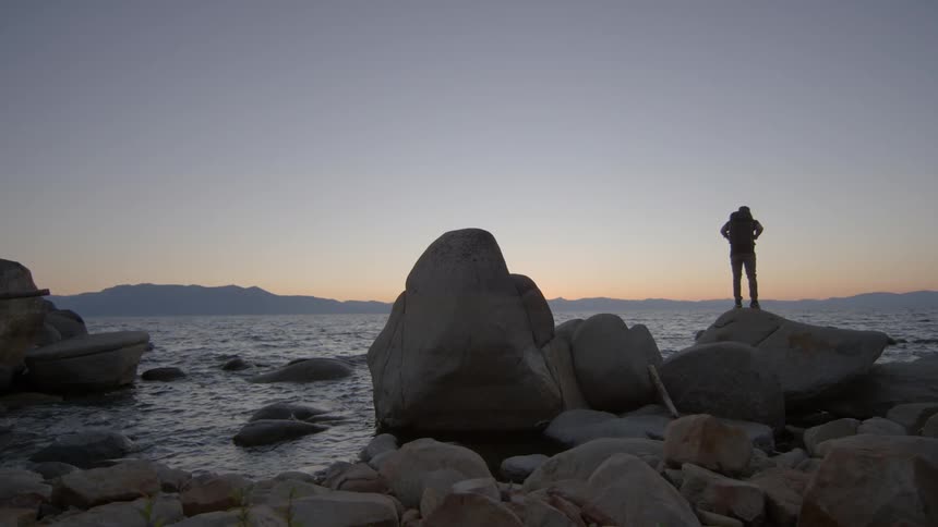 A man stands on top of boulders at the beach