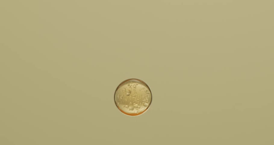 A droplet of yellow liquid slowly falling down against a tan background