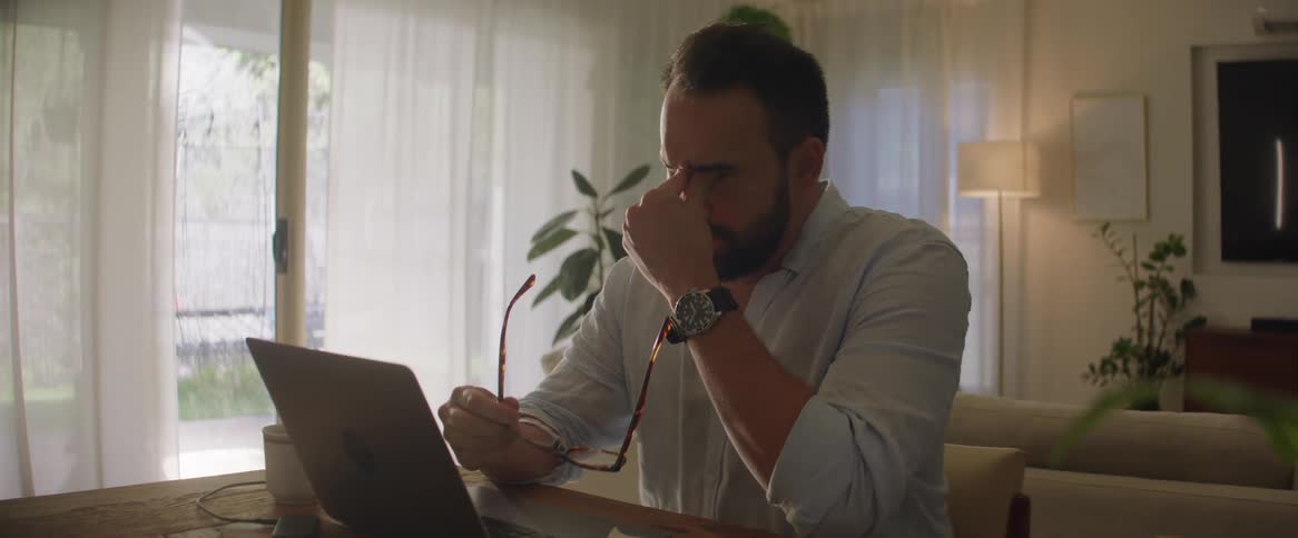 Man working from home briefly stops typing to rub his eyes