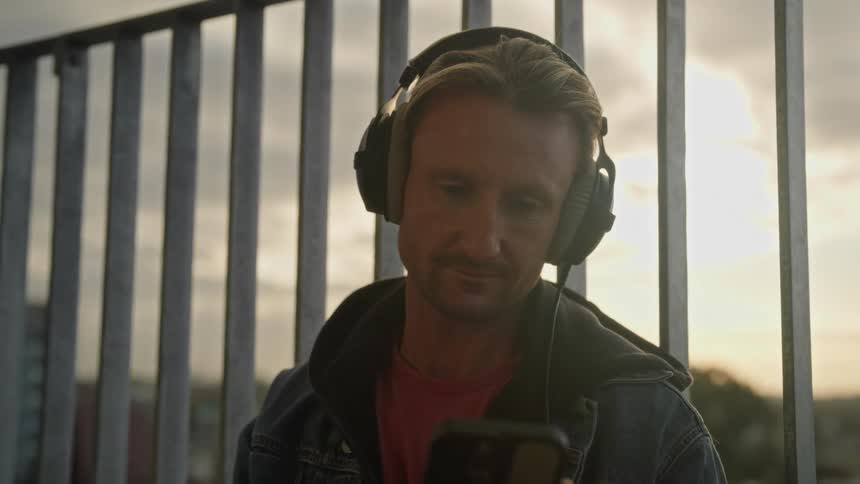 Portrait of a man with a happy facial expression on his phone and wearing headphones