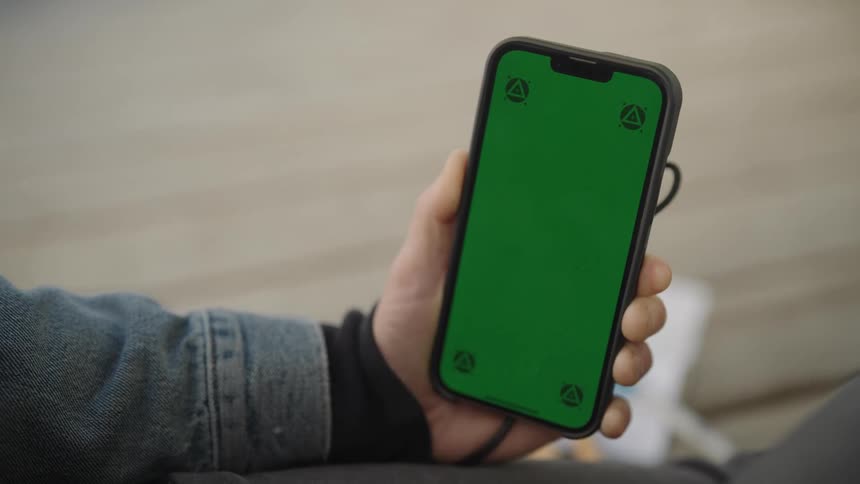 A persons hand holding a cellphone with a green screen on it