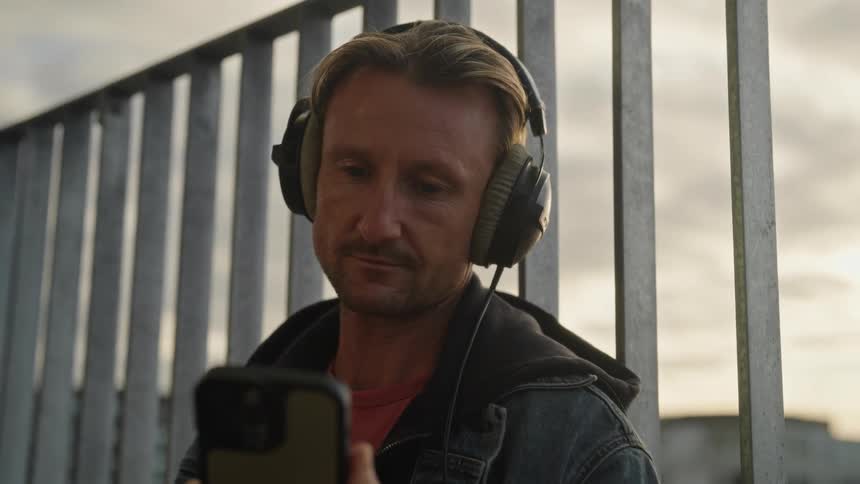 A man operating a mobile phone while standing near a metal fence at sunset