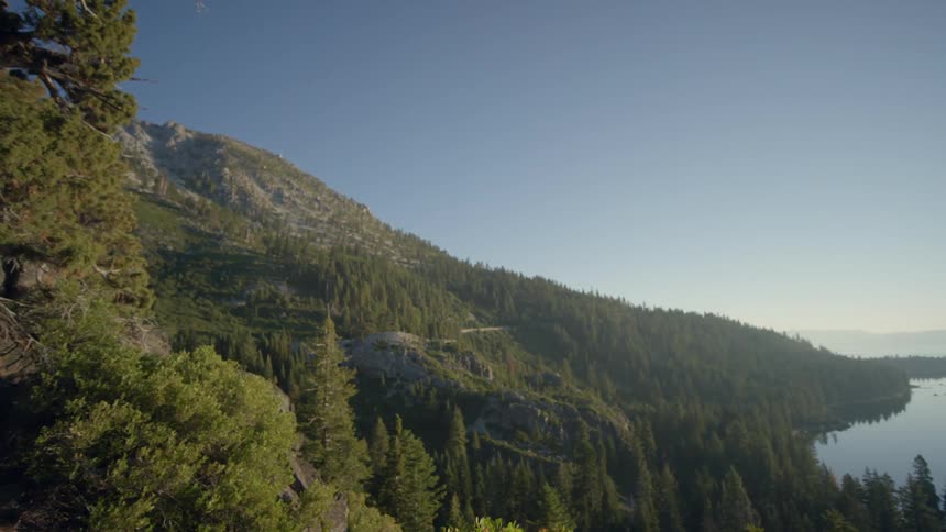 The mountain is covered with grass and trees with a lake below