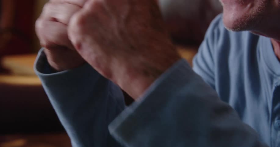 An older mans hands clapping as he cheers and smiles wearing a long sleeve blue shirt
