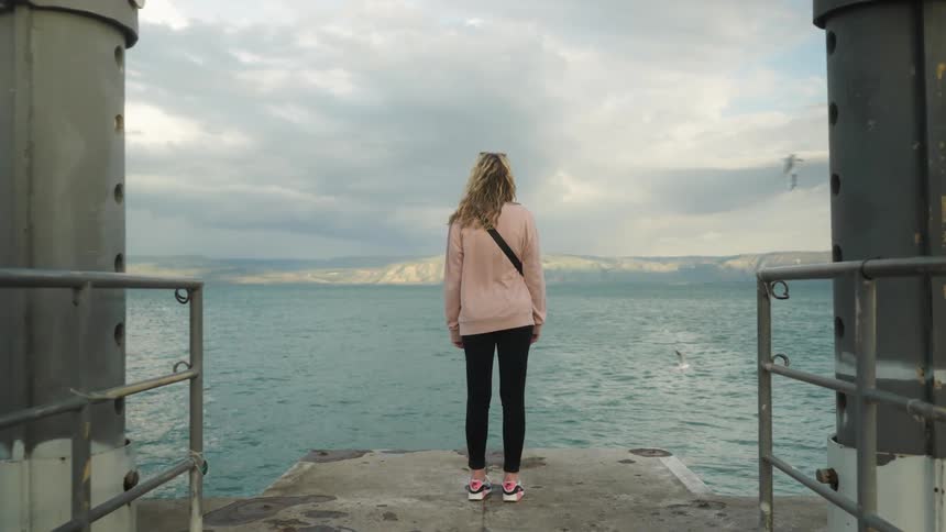 Lady stands on the dock facing the sea