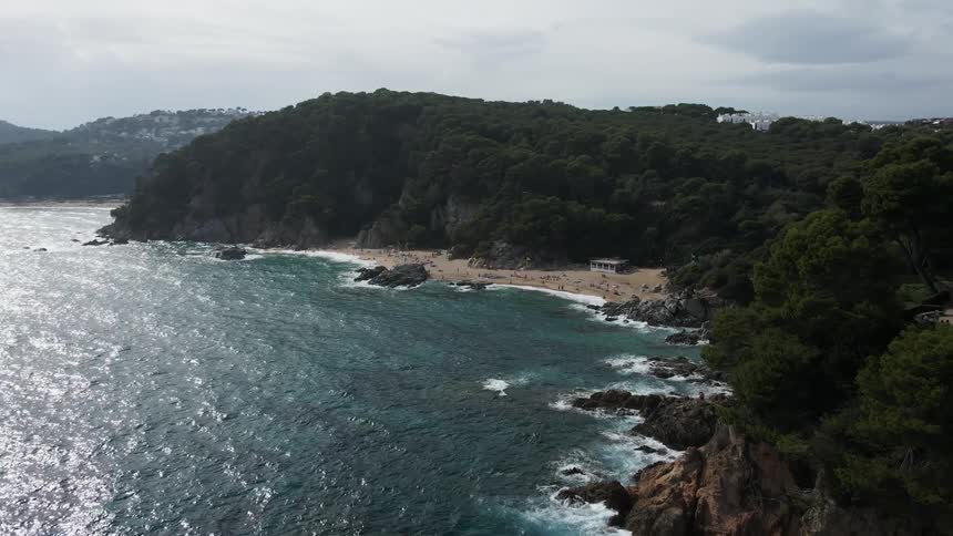 People enjoy beach at base of forested mountain topped by homes a distance from town