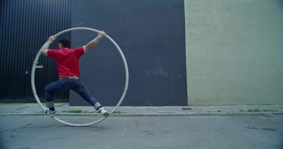 A man rolls past on a giant hoop on a city street