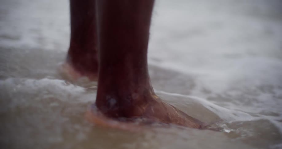 Close up of waves lapping around a person's feet in the sand