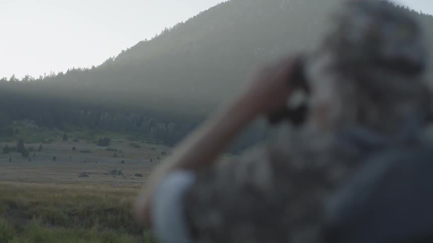 A man is using binoculars to view a mountain ahead