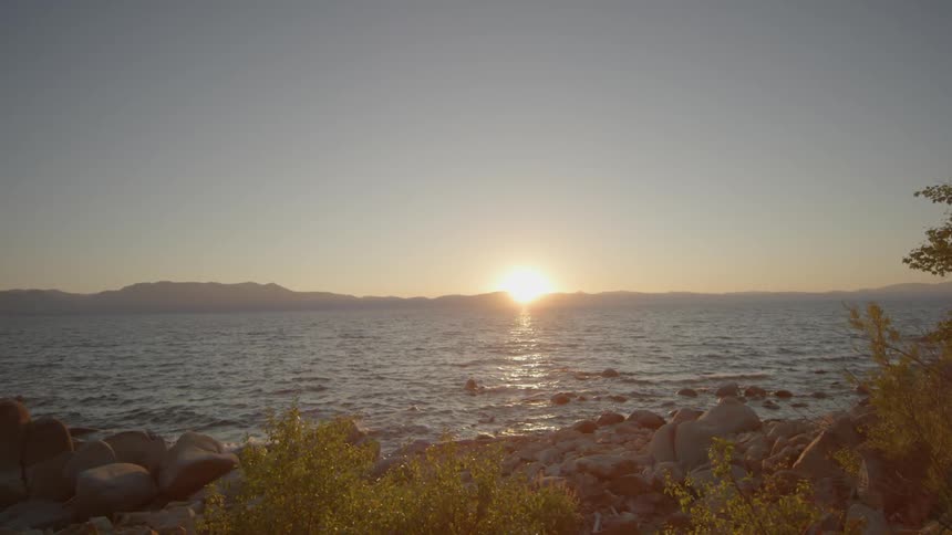 Grass and rocks lead to a lake at sunset