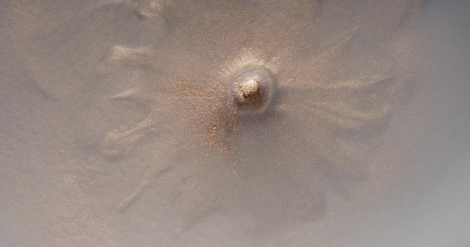 A drop of liquid falling on a surface filled with sand and sharps