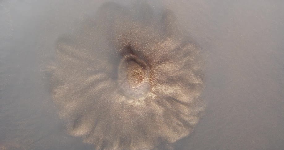 Sand emerges from beneath disturbed cloudy water