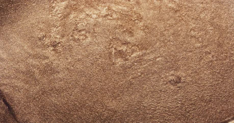 An organic golden dust ripples and wavers as it spreads outward across a rough surface