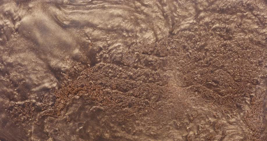 An organic golden powder ripples and flows as it moves across a rough surface