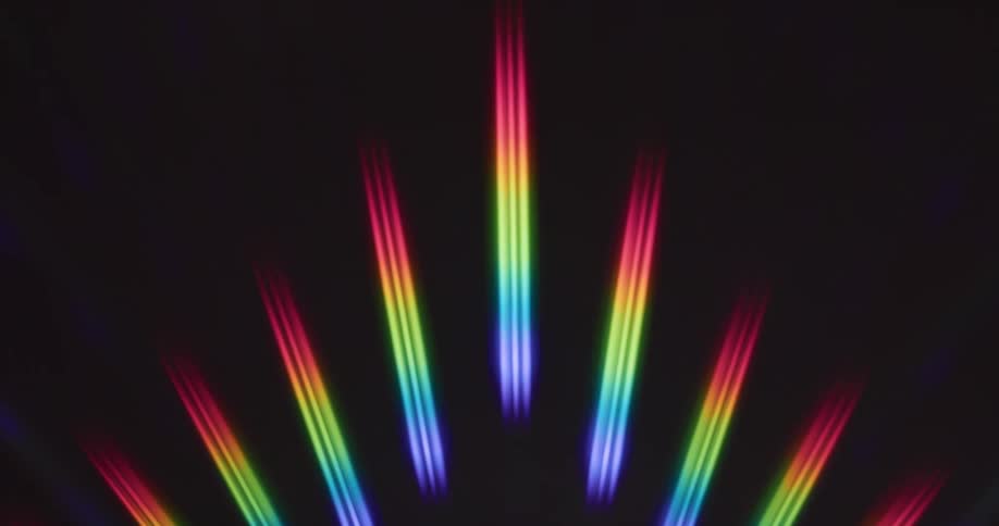 Glowing rainbow colored stripped bars of light are spread out in an arc and shine in the darkness as they move