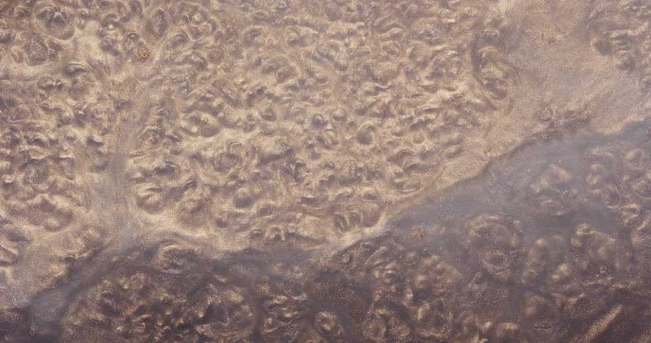 Dense liquid mixed with abstract golden sand in a boiling motion