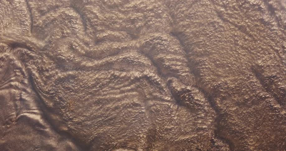 Golden glitter and sand with water flowing over it creating ripples and lines in the material