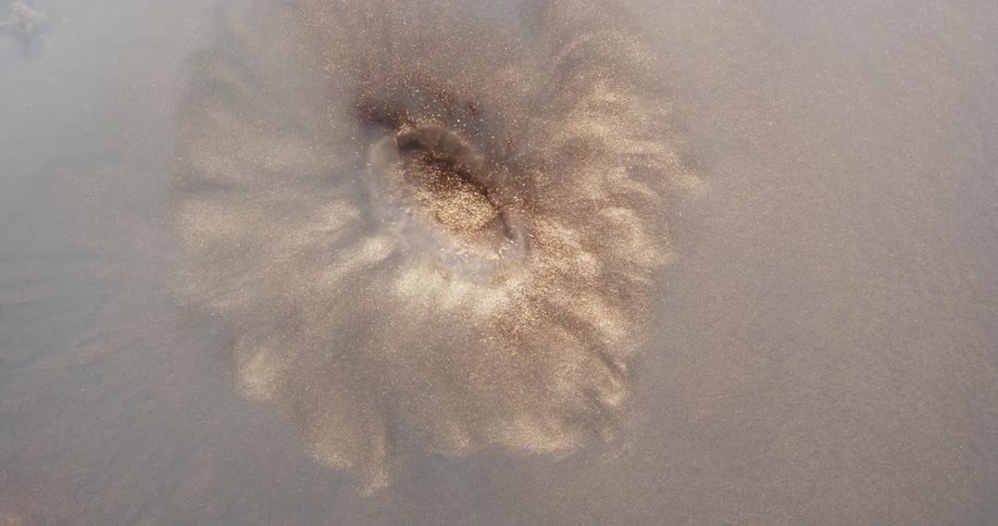 Water droplet falling on shiny sand creating an abstract impact