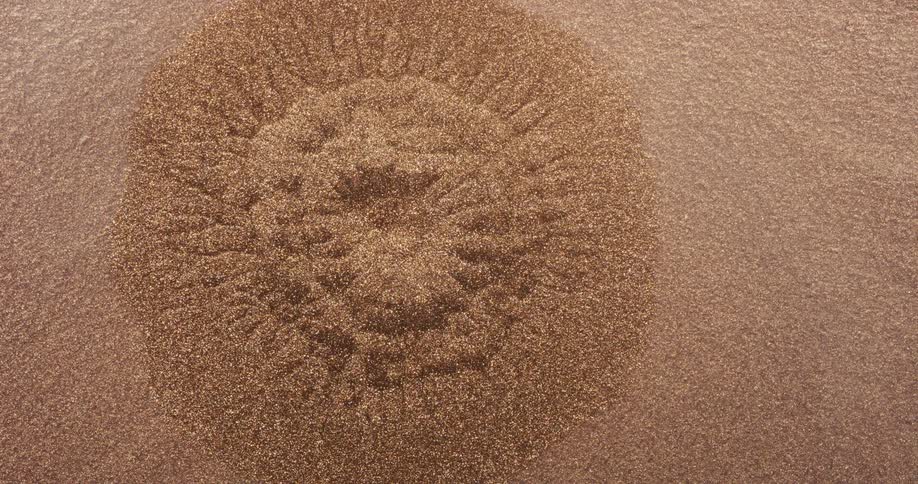 Water is dropped onto a pile of gold glitter as it sinks and creates a hole