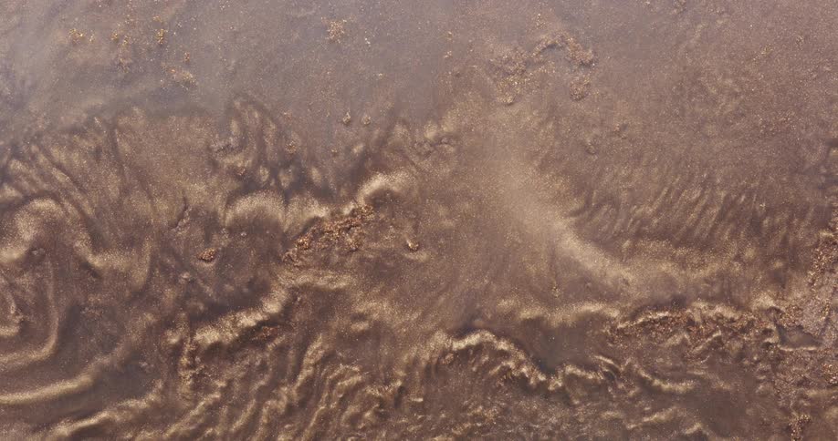 An organic golden dust ripples as it spreads across a rough surface