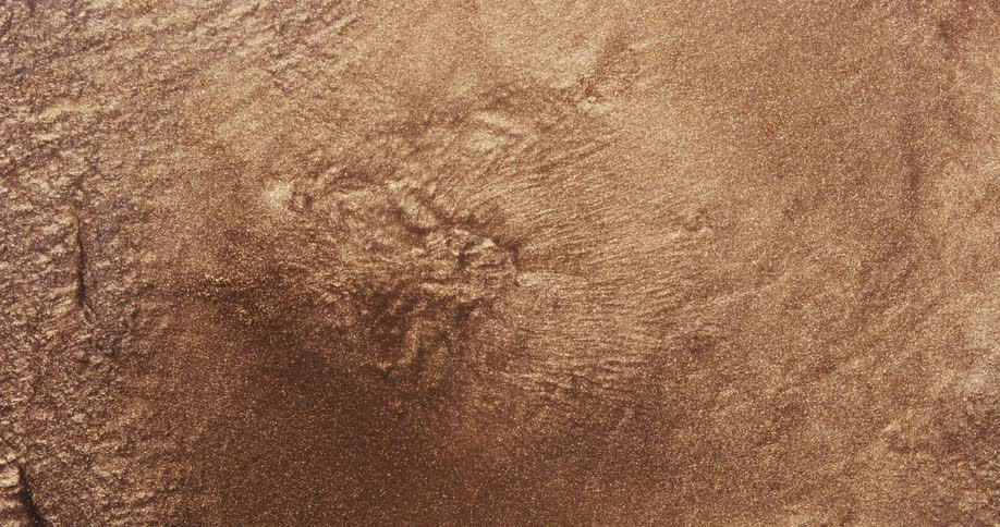 Liquid sinks into the center of metallic gold sand and flows toward the edge