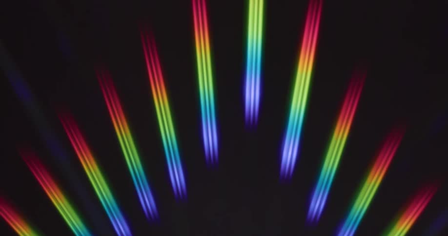 Glowing rainbow colored stripped bars of light are spread out in an arc and shine in the darkness as they move