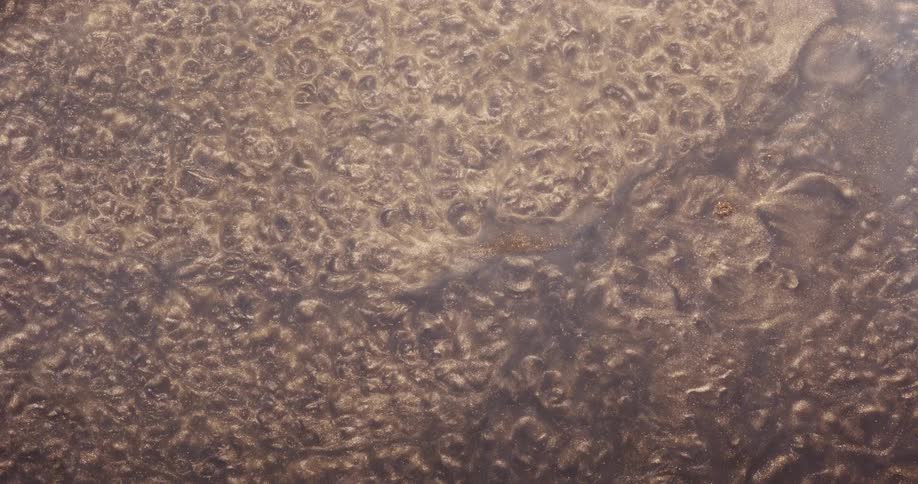Waves flow across the surface of pale lavender liquid