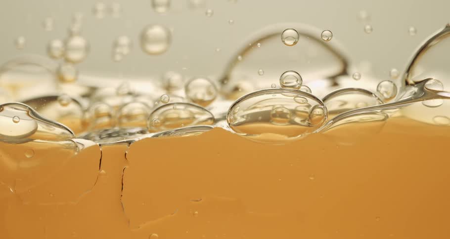 An amber colored liquid moves as bubbles rise and float in the substance