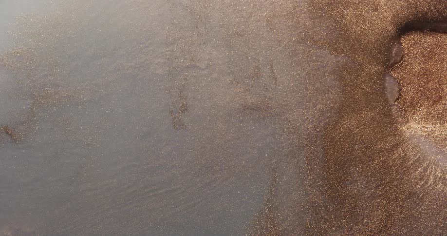 Gold and brown glitter particles flowing and rippling on a liquid