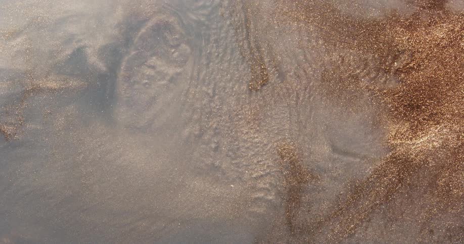 Liquid moves over a glittering gold powder and ripples as it covers a rough surface