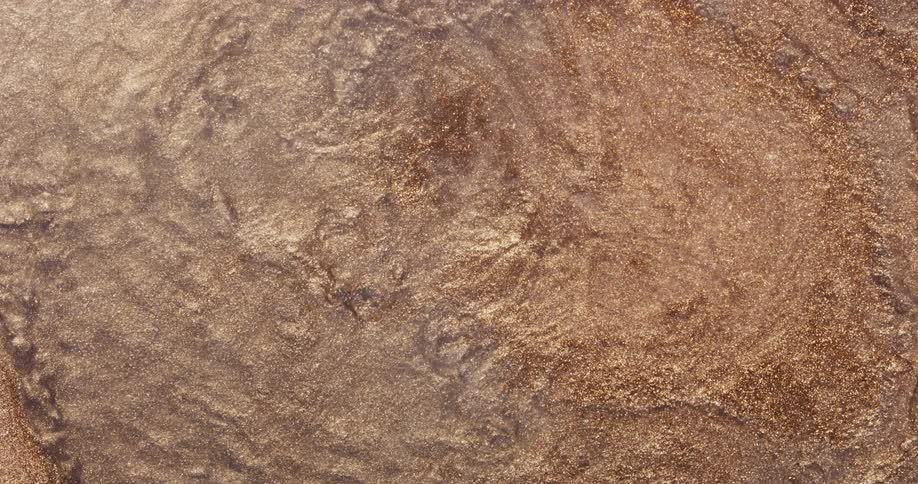 A glittery golden textured organic liquid moves over a rough surface as it spreads