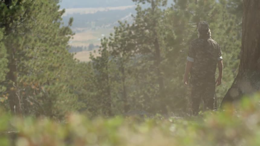 A man wearing camouflage stands before a forest