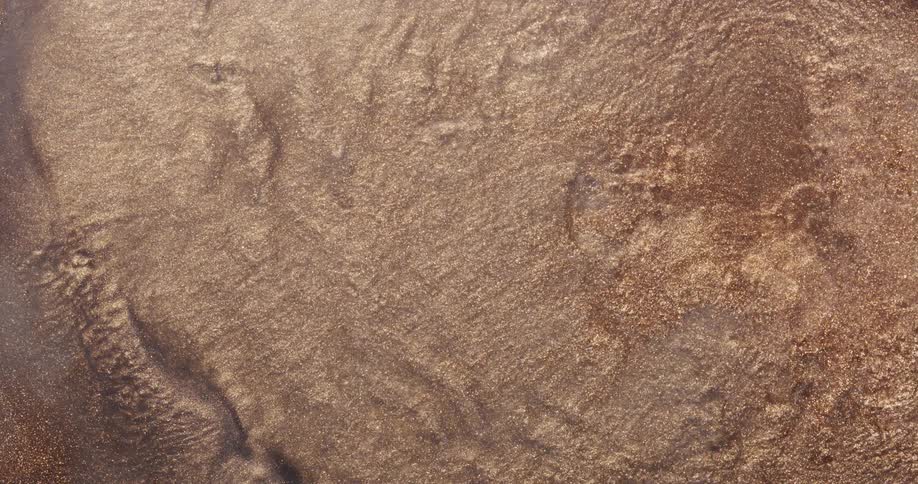 An organic golden dust ripples and wavers as it moves outward across a rough surface