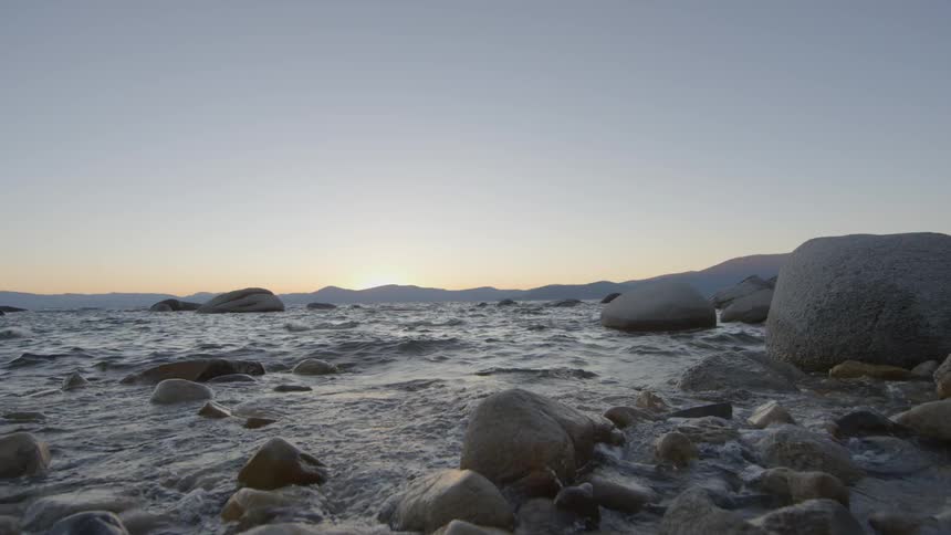 The waves crash against the rocks on the shore