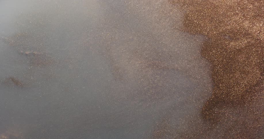 Gold shimmering particles sparkle near a white translucent liquid