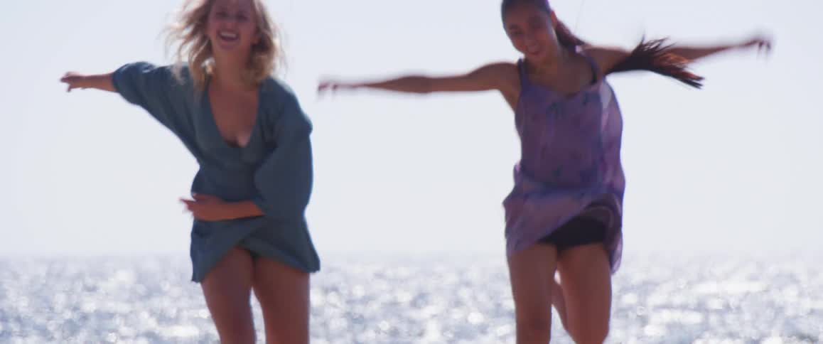 Two friends running on the beach smiling and happy