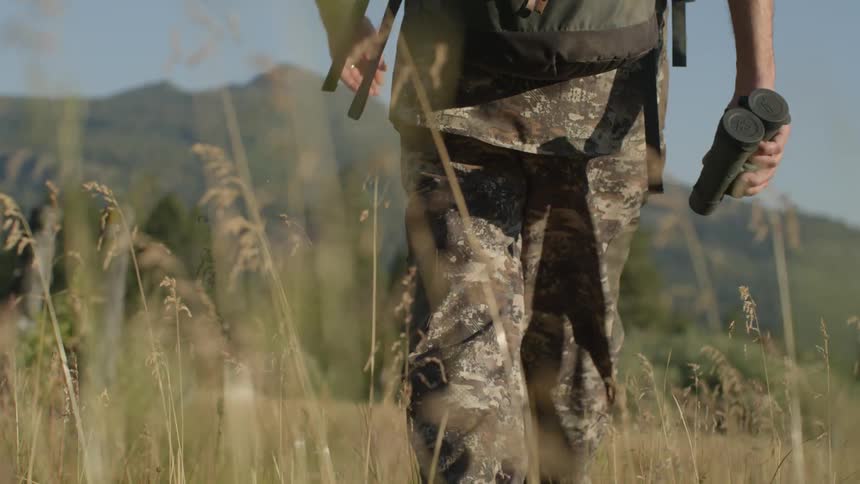 A man is hiking in tall grass carrying binoculars