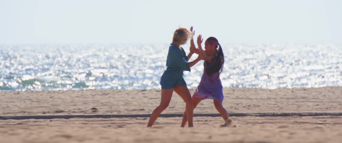 A couple of women perform choreography in front of the ocean