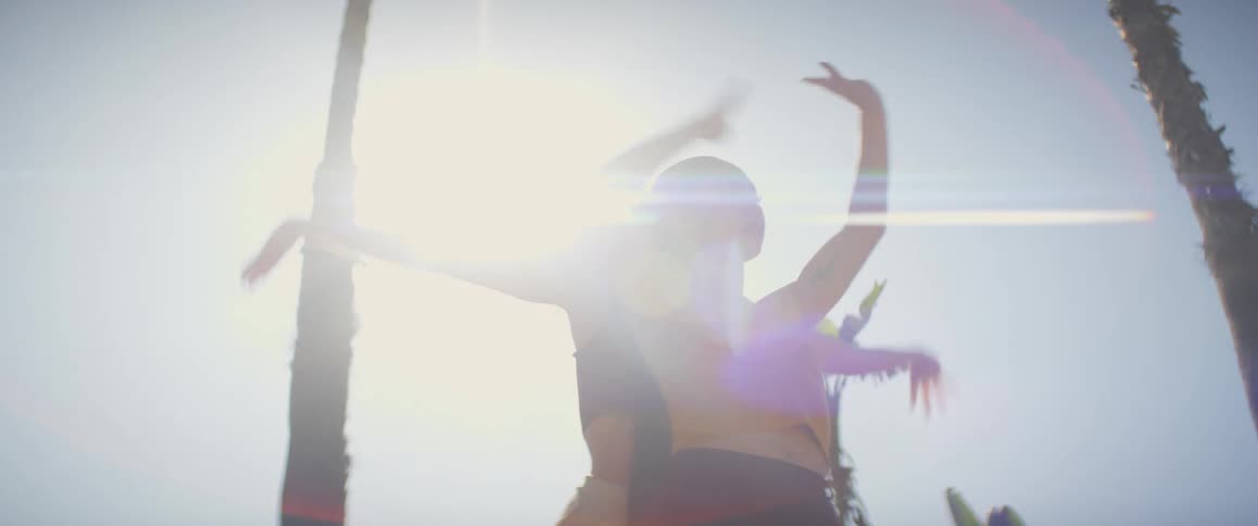 Two women dance outdoors near palm tree