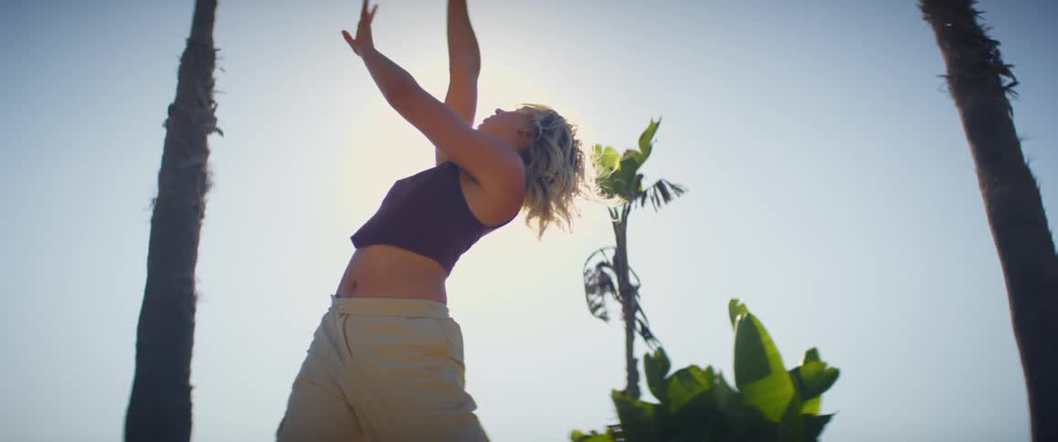 Young woman dances gesturing with her arms under the sun