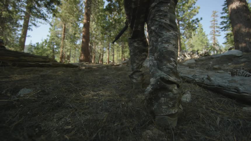 A man is hiking uphill carrying a rifle