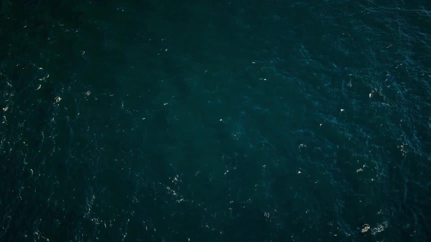 An aerial view of ocean waves and ripples creating foam on the surface