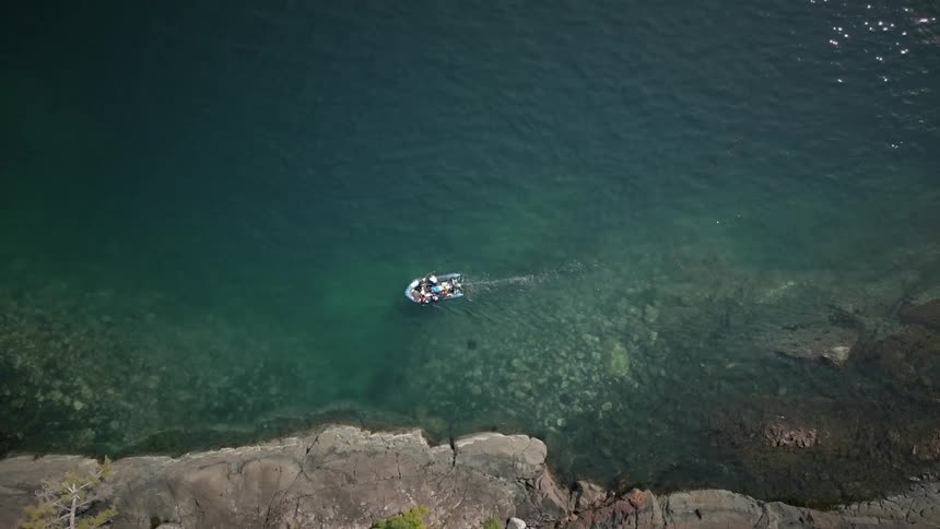 People ride boat through shallow coastal waters near stone shore