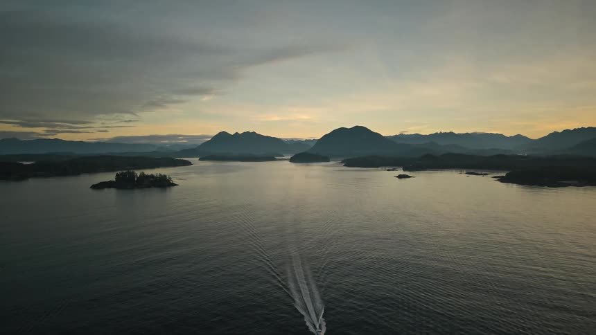 Boat leaves wake as it crosses water away from red tinted horizon and foggy terrain