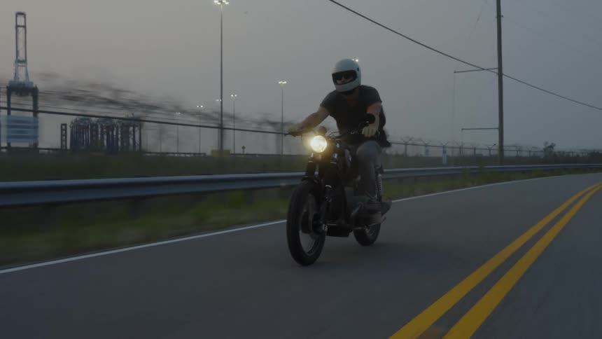 Man riding a motorcycle on the road in the early evening