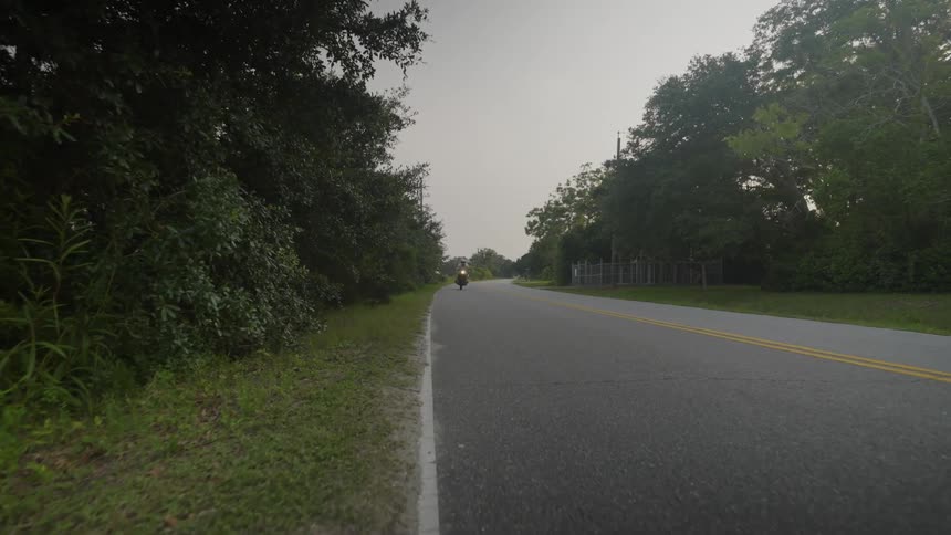 A motorcycle speeds on a quiet rural road surrounded by trees and woods