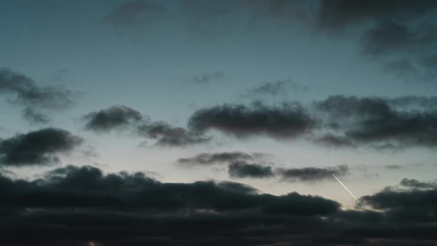 Dark clouds move across the sky as the white contrail of a missile streaks through